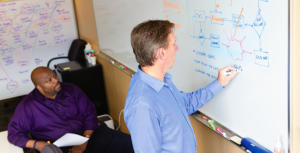 Eke and a coworker discuss process improvement ideas in his office