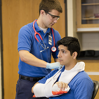 Male student practicing putting another student's arm in a sling