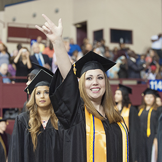 A female student in her cap and gown, holding up her hand
