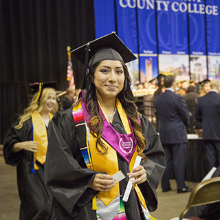 A female student smiling at the camera after receiving her diploma