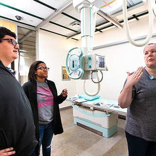 a female radiologic technology instructor showing a male student and a female student how to use a piece of radiology equipment