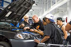 An instructor showing students different parts of a car engine