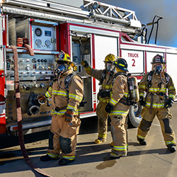 Students in fire fighting gear next to a fire truck