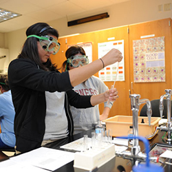 Students in a lab wearing protective googles measuring chemicals