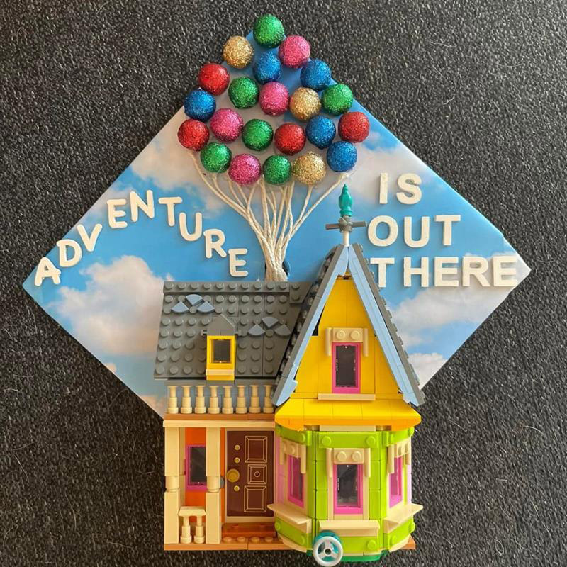 Graduation cap decorated with the house from the Pixar movie Up, accented with the text Adventure is Out There.