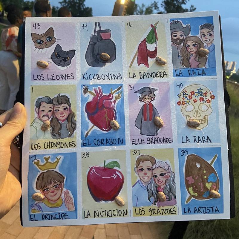 Graduation cap decorated with colorful loteria-style icons, including Los Leones, Kickboxing, La Bandera, La Raza, Los Chingones, El Corazon, Elle Graduade, La Rara, El Principe, La Nutricion, Los Grandes and La Artista.