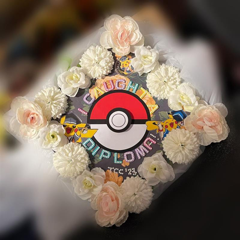 Graduation cap with white flowers around the edges and a pokeball in the center, surrounded by graduating pikachus and the text I caught a diploma!