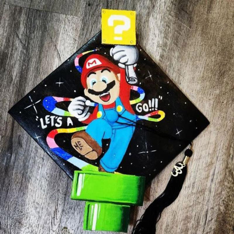 Graduation cap with Nintendo's Mario jumping out of a tunnel and showing Let's a go!