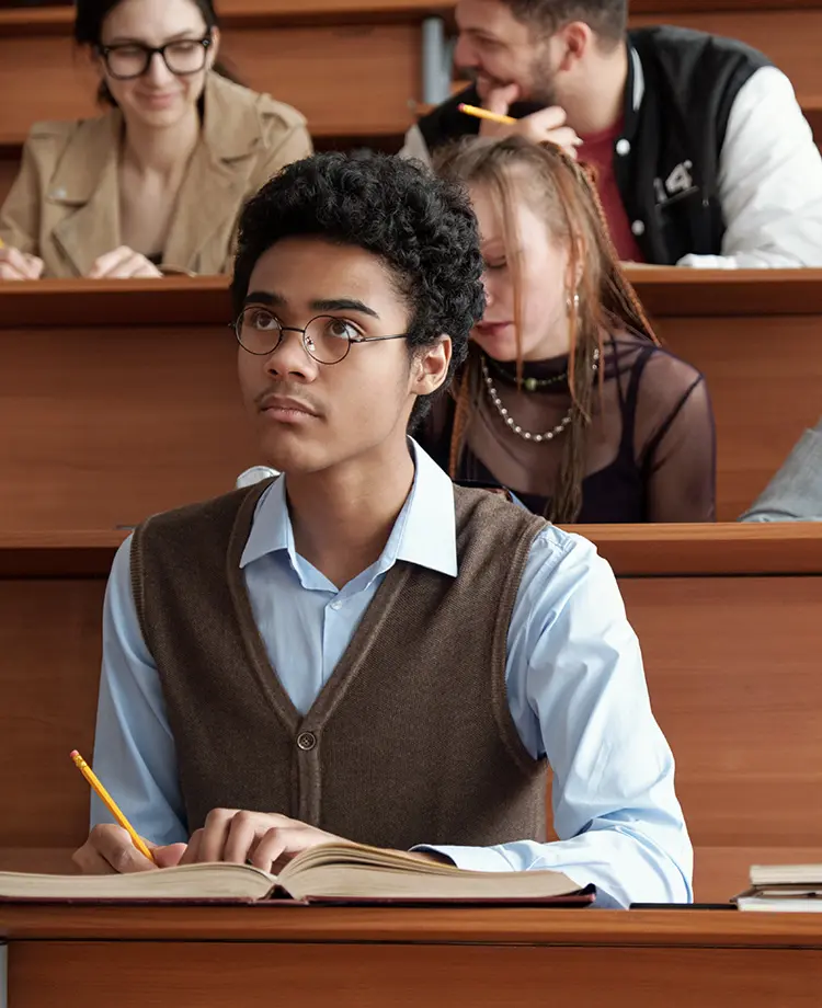 A student in glasses and a vest looks up from their notes