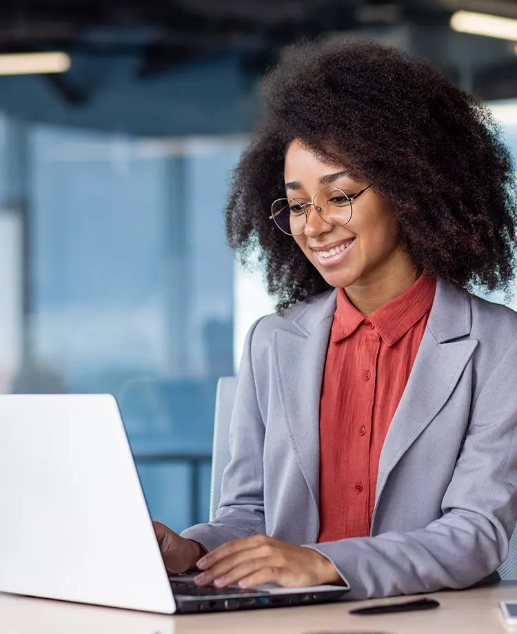 A student in glasses with large naturally curly hair in a smart blazer works on a laptop