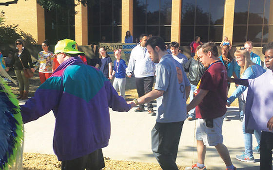 Students standing outside in a large circle, holding hands.