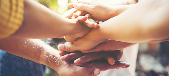 A crowd of people all putting their hands together in a circle, signaling teamwork