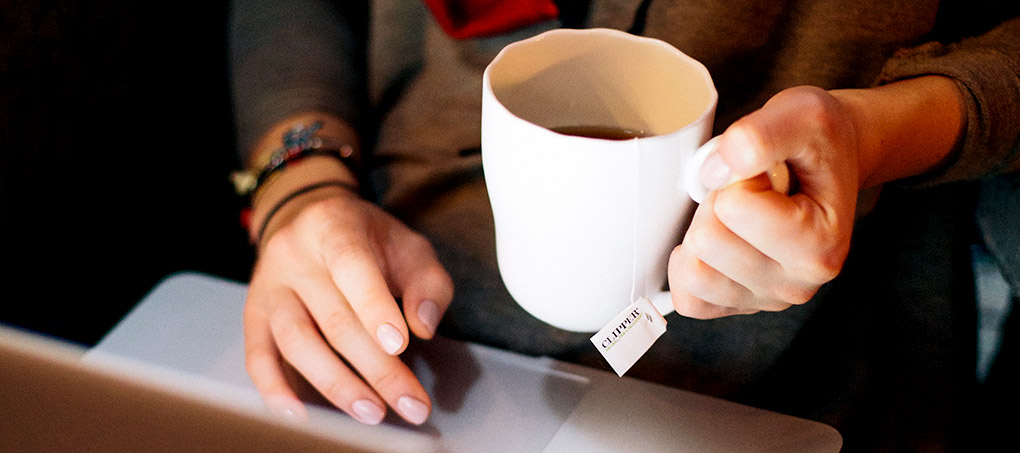 A student holds a mug of coffee and works on a laptop