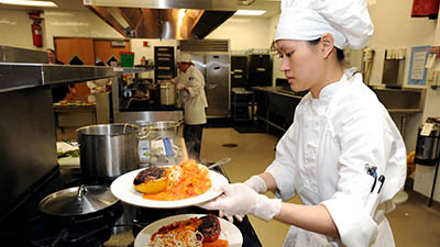 A student in chef's whites plates a gourmet dish