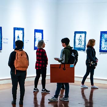 Standing students studying artwork on the walls in the Carillon Gallery.