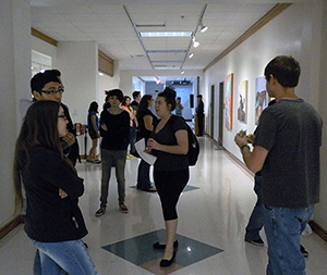 View looking down the hall during an art exhibition: Scattered vistors view art on the walls on either side of the hallway.