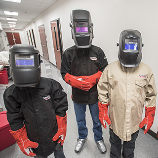 three welding students wearing protective clothes and head gear
