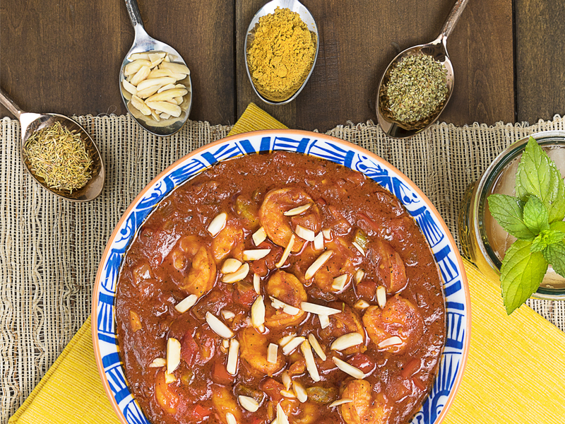 Bowl of Bajan Shrimp Curry surrounded by spoons of herbs included in the recipe