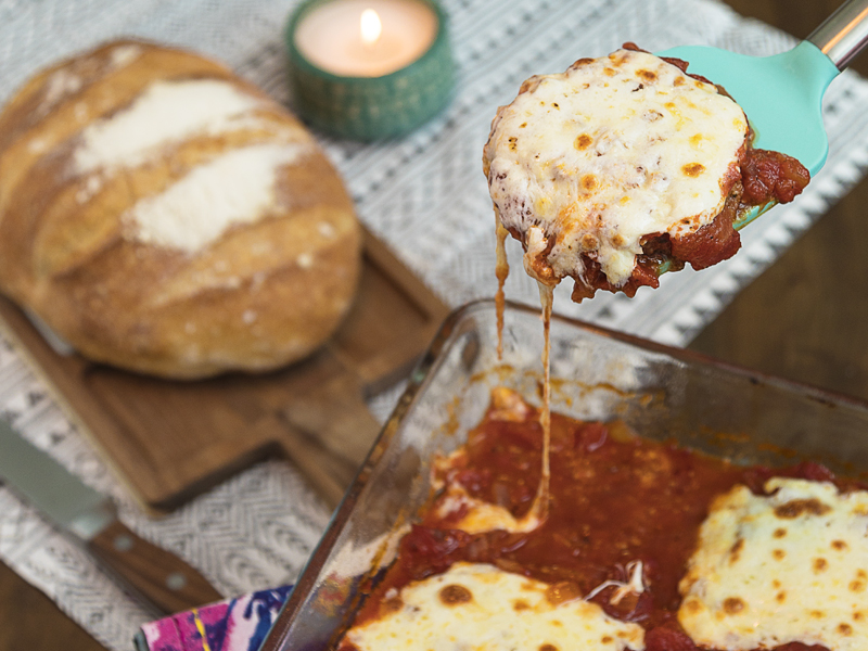 Serving of eggplant pomordoro on a spatula, the rest of the casserole and a loaf of bread in the background