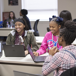 Three young girls sitting around a table with laptops