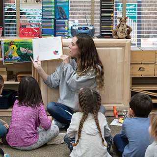 A woman reading a storybook to young children