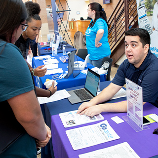 at a student organization fair, 2 female students talk to a male representative of the Go Center Mentoring program