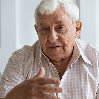 a white-haired man telling a story and gesturing with his right hand