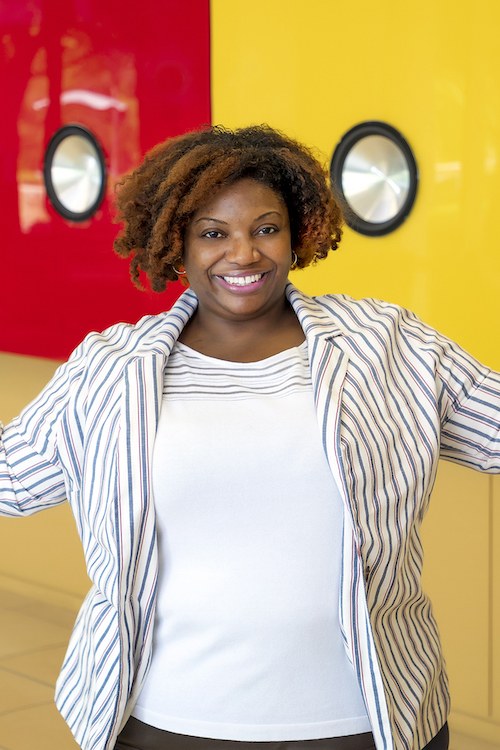 Arlene Peterson stands with her arms spread open in front of a vivid red and yellow background