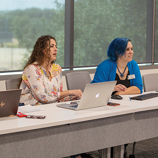 Two women sitting at a table with their laptops