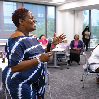 woman standing up talking into a microphone in front of faculty