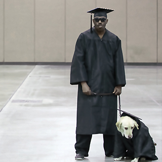 Graduate with sunglasses holds his guide dog at graduation