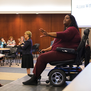 Tracy Jordan sits in her wheelchair on a stage and speaks to a crowd.