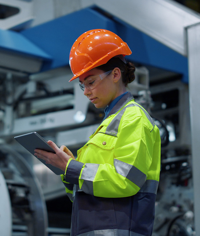 A woman in a high-vis vest and hard hat looks at a tablet computer. She received a technical certificate from TCC, allowing her to advance her career