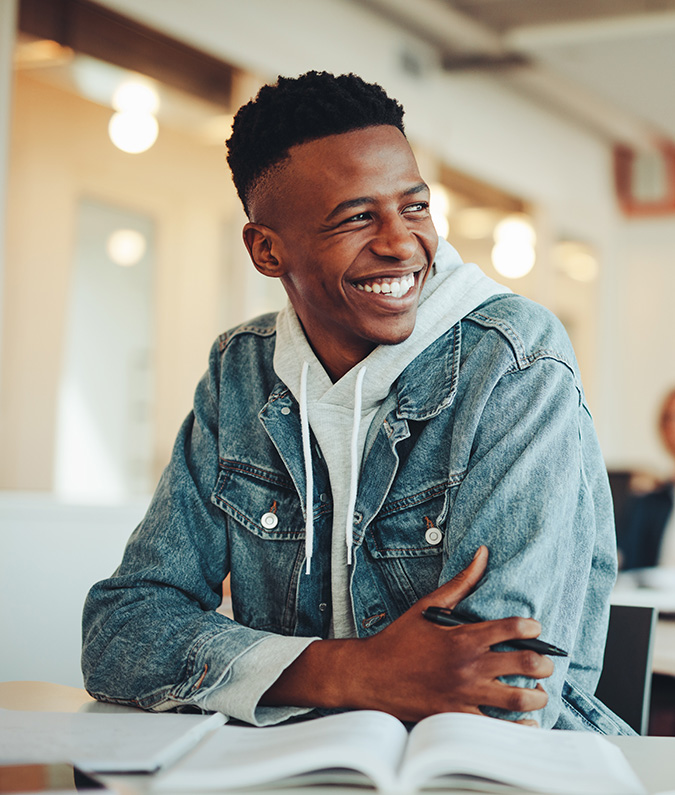 A young man in a denim jacket smiles joyfully, because he’s starting off his college journey with an associates degree he earned in a TCC dual-credit program